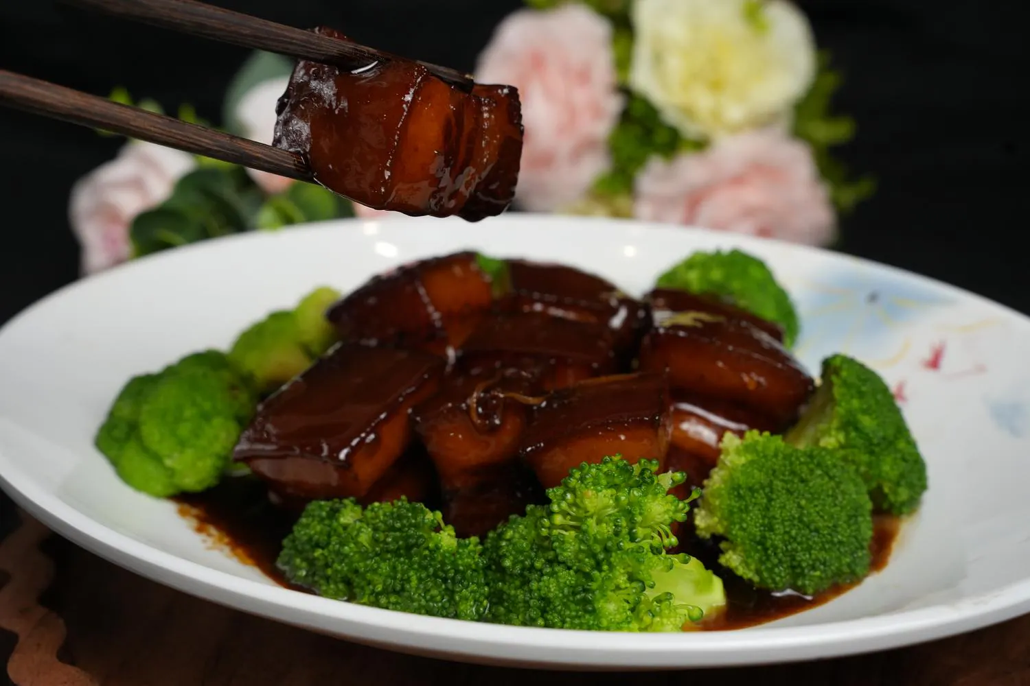 A chunk of glazed braised pork belly held by chopsticks